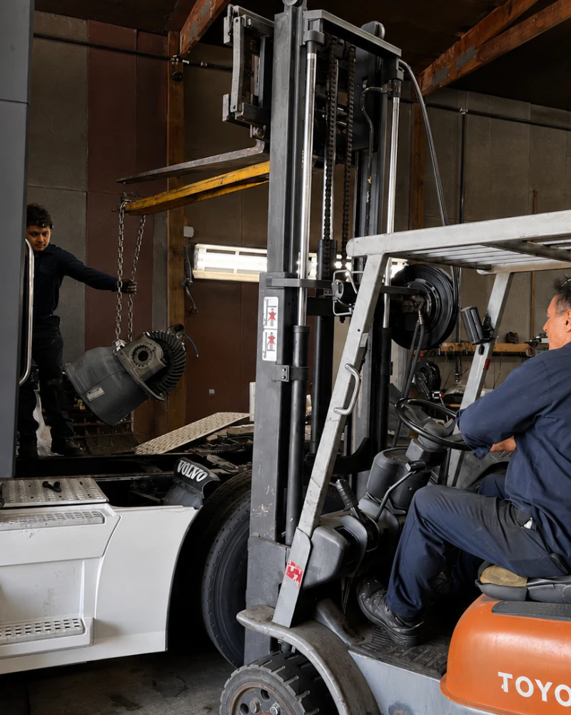 Two technicians moving a heavy truck component with a forklift at Big Truck & Trailer Repair in Park City, Illinois